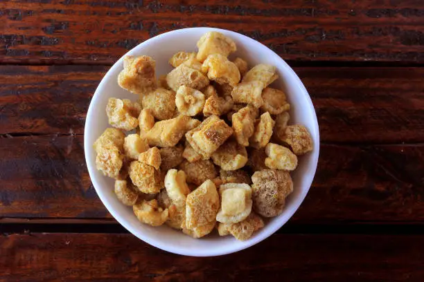 Photo of pork rinds (torresmo) fried in ceramic bowl on rustic wooden table in restaurant. typical dish of Brazilian and Asian cuisine