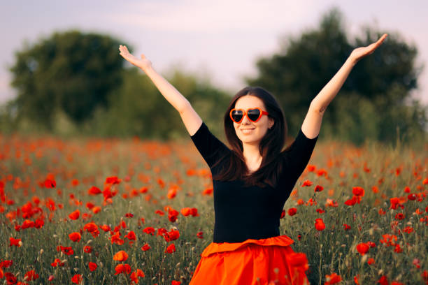 Happy Woman with Heart Shaped Sunglasses Enjoying Nature Relaxed girl having fun in summer outdoors in a flower field white shirt black skirt stock pictures, royalty-free photos & images