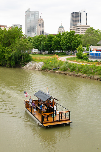 Fort Wayne, Indiana, USA - June 8, 2019: Barge Bar, carrying people drinking, traveling on St Marys River, with city skyline at the background