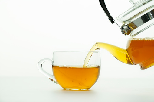 Pouring tea from teapot to tea glass on white background