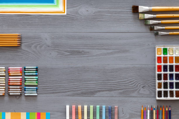 istock Creative art table background with watercolor paints palette paintbrushes pencils crayons supplies tools on grey wooden desk, artist gray design workspace top view from above, flat lay, copy space 1155126124