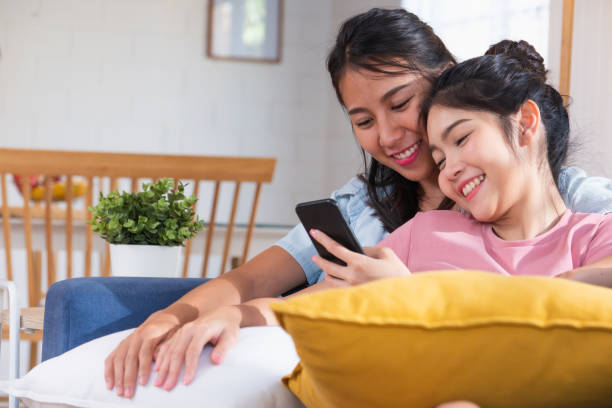 счастливый азиатских лесбиянок смотреть видео на мобильный телефон на диване в доме. концепция образа жизни лгбт. - bff стоковые фото и изображения