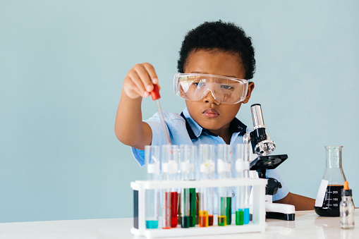 Serious African American boy in protective goggles using pipette while trying to learn how to mix colorful chemicals in laboratory