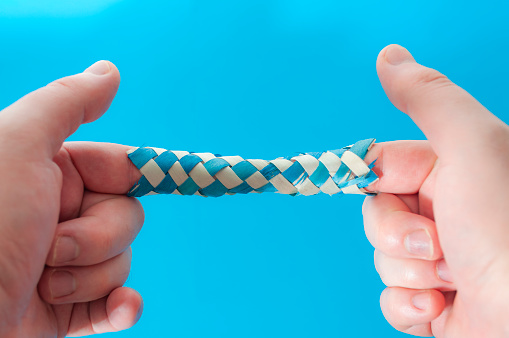 Puzzle game and logic games concept with hands playing with a chinese finger trap, a toy that the more you pull the tighter it gets stuck and you need to push to escape isolated on blue background