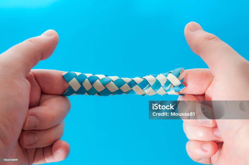 Puzzle game and logic games concept with hands playing with a chinese finger trap, a toy that the more you pull the tighter it gets stuck and you need to push to escape isolated on blue background Trapped Stock Photo