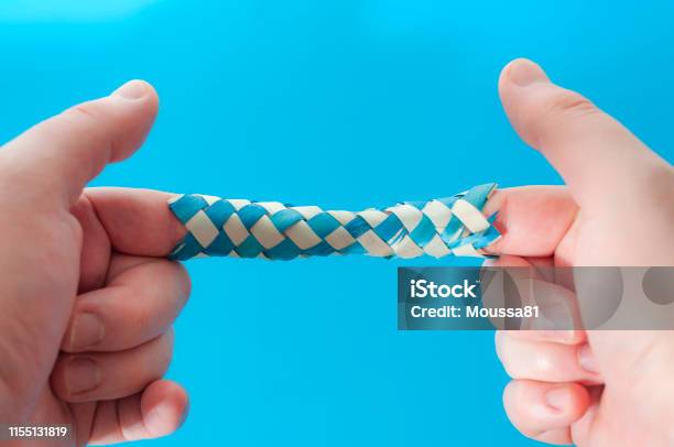 Puzzle Game And Logic Games Concept With Hands Playing With A Chinese Finger Trap A Toy That The More You Pull The Tighter It Gets Stuck And You Need To Push To Escape Isolated On Blue Background Stock Photo - Download Image Now