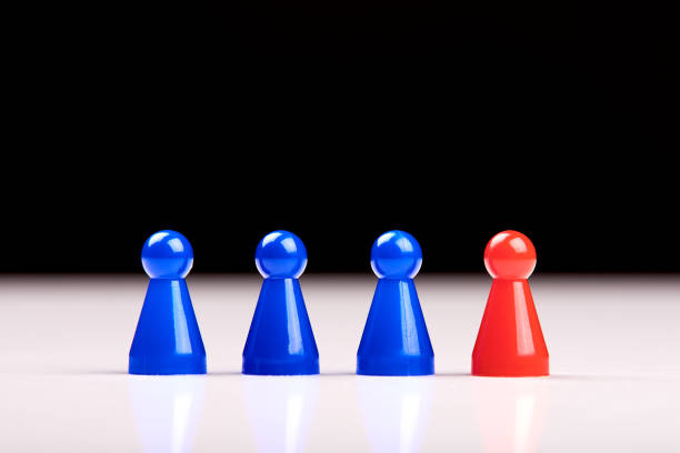 istock Three blue game pieces and a red figure standing next to them as a leader, boss or different. Blurred black and white background. 1155136387