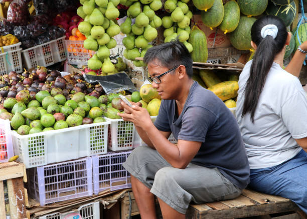 Indonesian man sitting and using mobile phone in front of fruit shop at the fresh market in Jakarta. stock photo