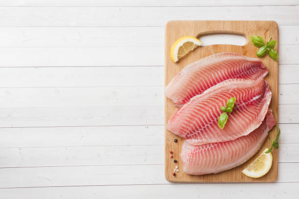 istock Raw fish fillet of tilapia on a cutting Board with lemon and spices. White table with copy space. 1155142011