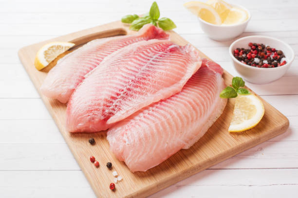 Raw fish fillet of tilapia on a cutting Board with lemon and spices. White table with copy space. Raw fish fillet of tilapia on a cutting Board with lemon and spices. White table with copy space pink pepper spice ingredient stock pictures, royalty-free photos & images