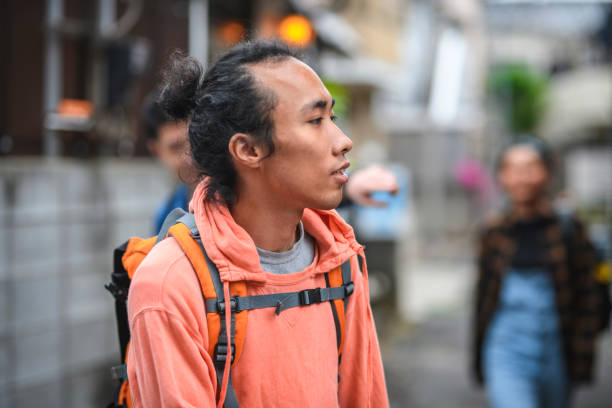 Close-up of young Japanese male backpacker on vacation and walking with friends through the streets of Tokyo.