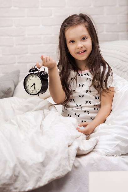 istock little child girl in pyjamas with clock 1155143423