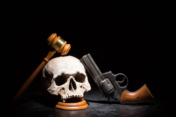 Legal law, justice and murderment crime concept. Wooden judge gavel hammer on human skull with revolver gun pistol against black background Legal law, justice and murderment crime concept. Wooden judge gavel hammer on human skull with revolver gun pistol against black background. gun laws stock pictures, royalty-free photos & images