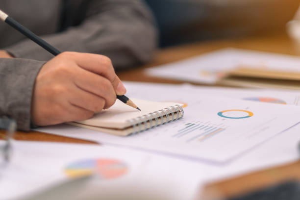 istock businesswoman writing on notebook and working on business data 1155160020