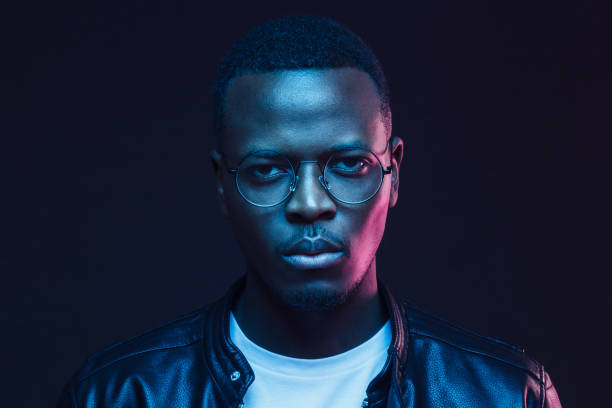 Portrait of serious African man wearing glasses and leather jacket at night Portrait of serious African man wearing glasses and leather jacket at night serious black teen stock pictures, royalty-free photos & images