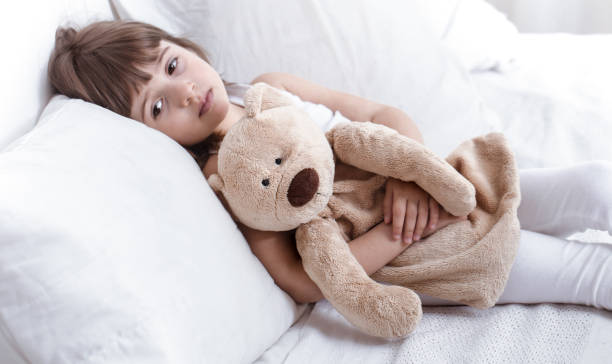 istock Cute little girl smiling while lying in a cozy white bed 1155161707