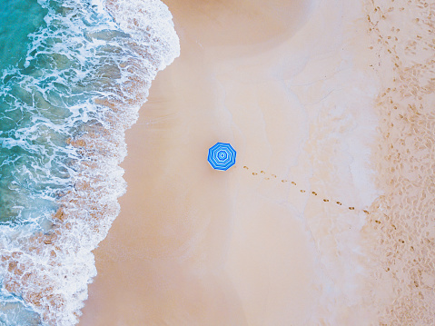 creative colorful shot of beach umbrella near ocean wave from above, minimalist landscape
