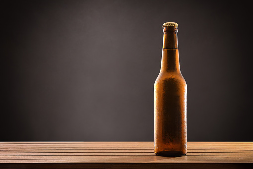 Beer bottle filled and closed on wood table and black background. Horizontal composition. Front view.