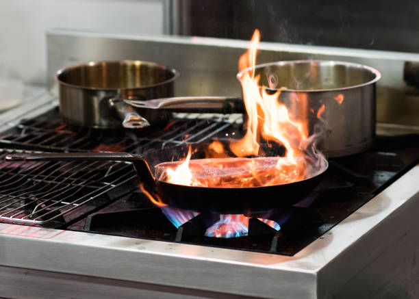 istock Chef cooking with flame in a frying pan on a kitchen stove 1155163781
