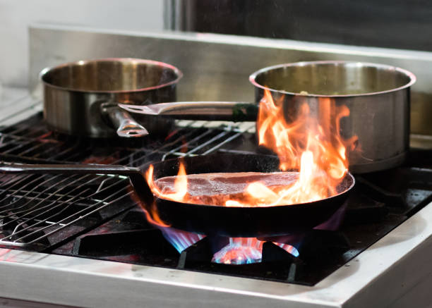 istock Chef cooking with flame in a frying pan on a kitchen stove 1155163797