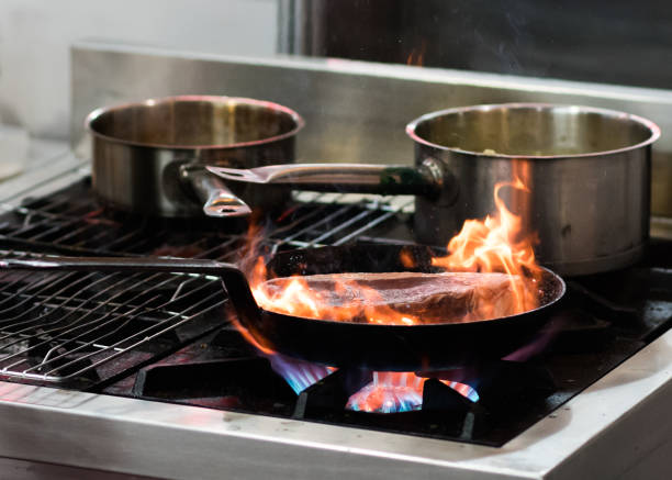 istock Chef cooking with flame in a frying pan on a kitchen stove 1155163819