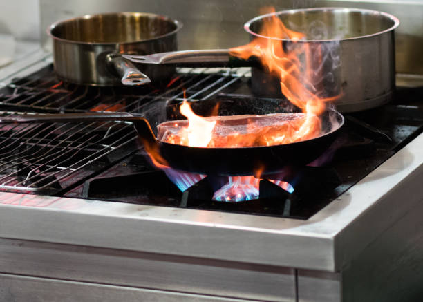 istock Chef cooking with flame in a frying pan on a kitchen stove 1155163909