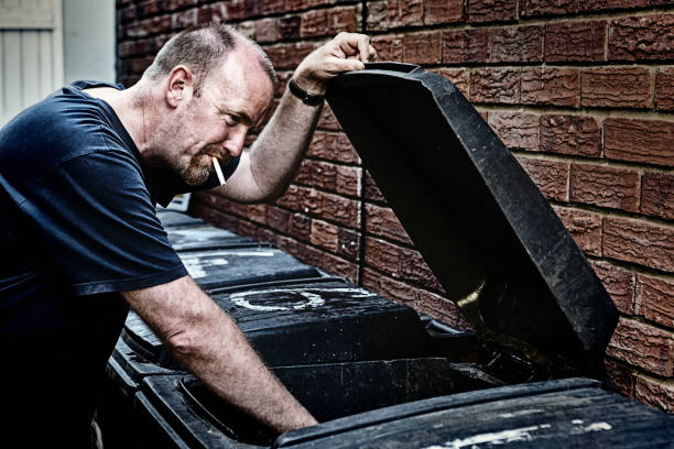 istock Mature male vagrant smokes, rummaging in refuse bin 1155163918