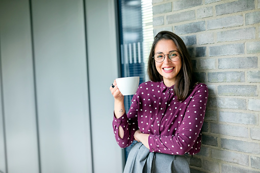 Portrait of a gorgeous young woman standing in her office with a coffee cup
