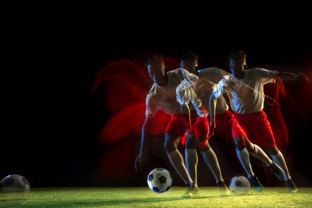 istock Male soccer player kicking ball on dark background in mixed light 1155164184
