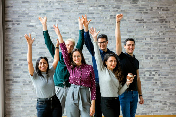 Happy business people celebrating success at office Shot of young businesspeople standing together with their hands raised and celebrating success at office organized group photos stock pictures, royalty-free photos & images