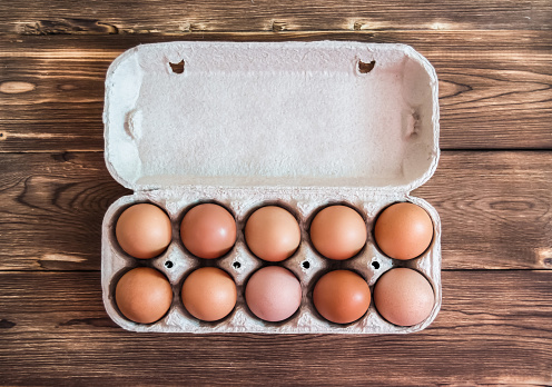 Chicken eggs in carton pack top view on brown wooden background
