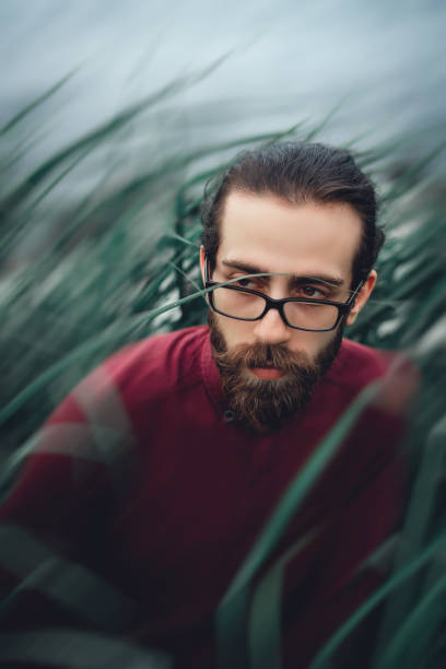 istock Young bearded handsome guy sitting in grasses 1155173880
