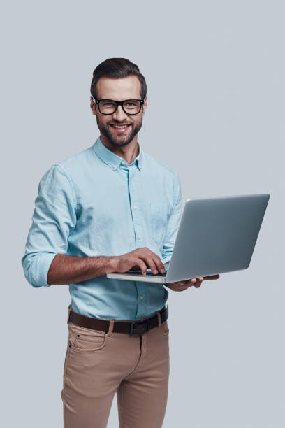 istock Looking for fresh ideas. Good looking young man carrying laptop and looking at camera while standing against grey background 1155174062