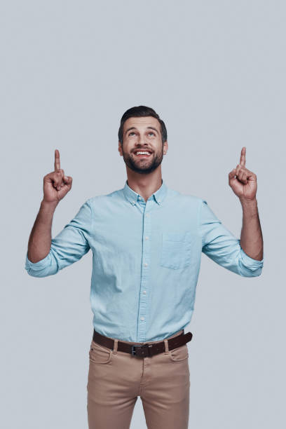 istock Look over there! Handsome young man pointing copy space and smiling while standing against grey background 1155174279