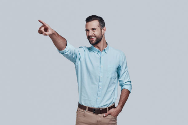 istock Look! Handsome young man pointing copy space and smiling while standing against grey background 1155174329