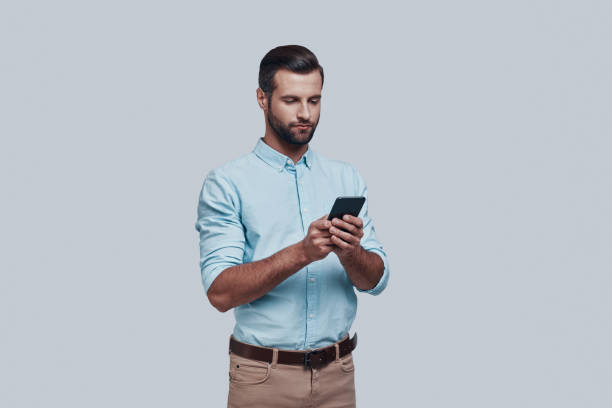 istock Important business message. Handsome young man using smart phone while standing against grey background 1155174490