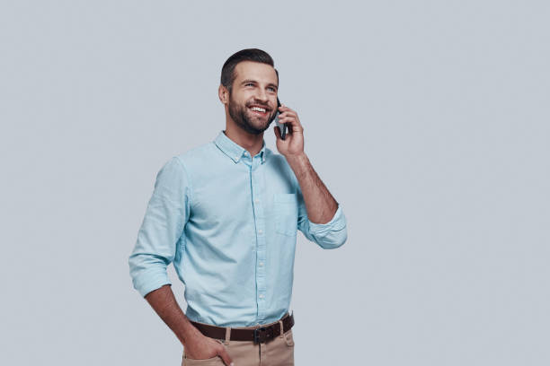 Talking about business. Handsome young man talking on the smart phone and smiling while standing against grey background