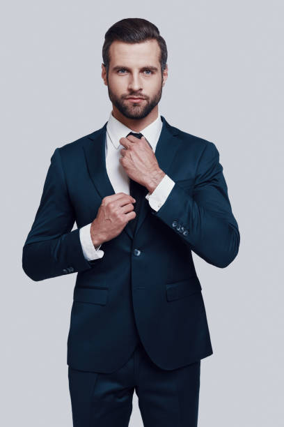 istock Good looking entrepreneur. Handsome young man looking at camera and adjusting his necktie while standing against grey background 1155175988