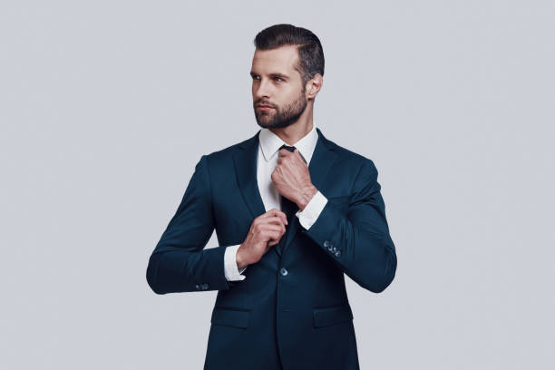 istock Getting ready. Handsome young man adjusting his necktie while standing against grey background 1155176024