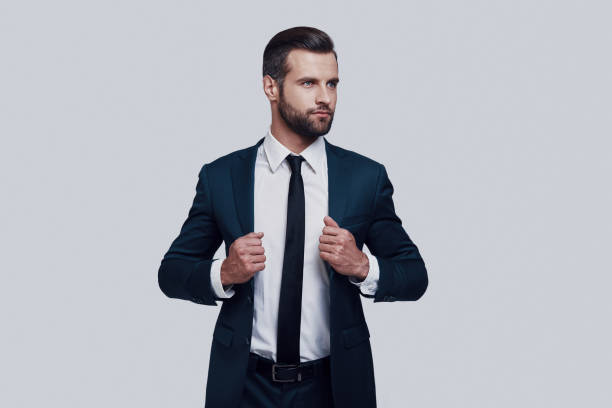 istock Young and successful. Handsome young man adjusting his jacket while standing against grey background 1155176056