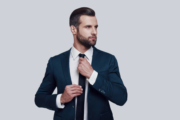 istock Getting ready to become the best. Handsome young man adjusting necktie while standing against grey background 1155177598