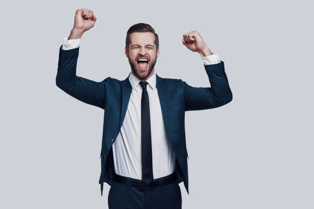 istock Success! Handsome young man cheering and smiling while standing against grey background 1155178014