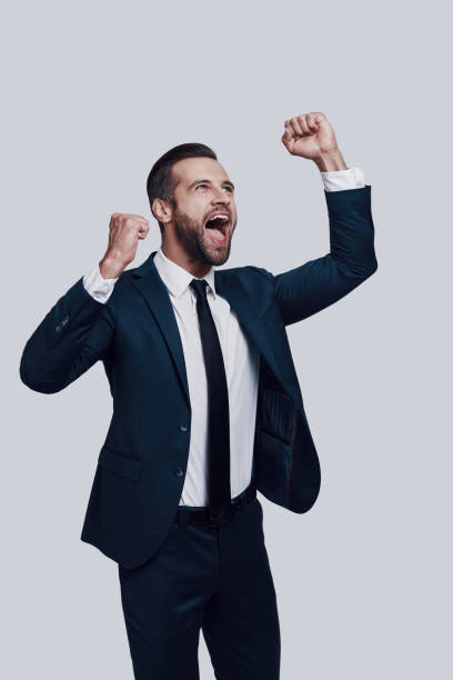 istock Winning! Handsome young man cheering and smiling while standing against grey background 1155178049