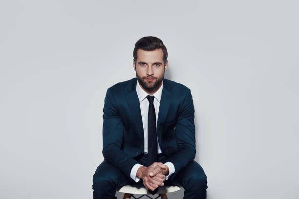 istock Perfect in every way. Handsome young man looking at camera while sitting against grey background 1155178110