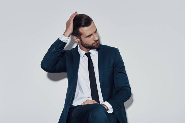 istock Moment to think. Handsome young man adjusting his hairstyle while sitting against grey background 1155178835