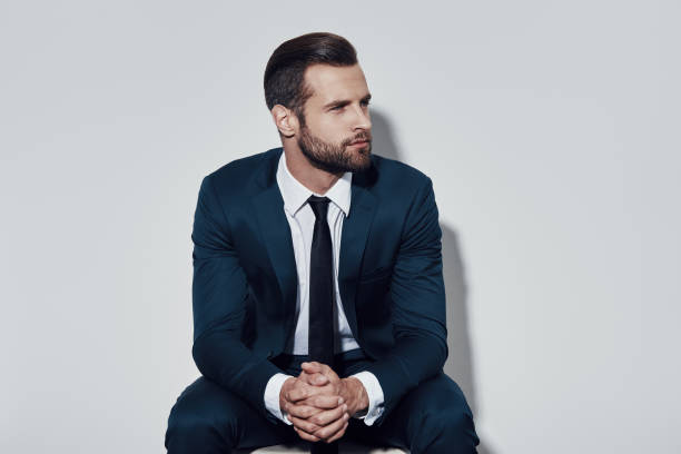 istock Time to make decision. Handsome young man looking away while sitting against grey background 1155179052