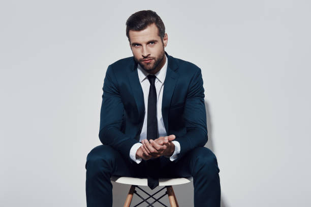 istock Contemplation. Handsome young man looking at camera while sitting against grey background 1155179208