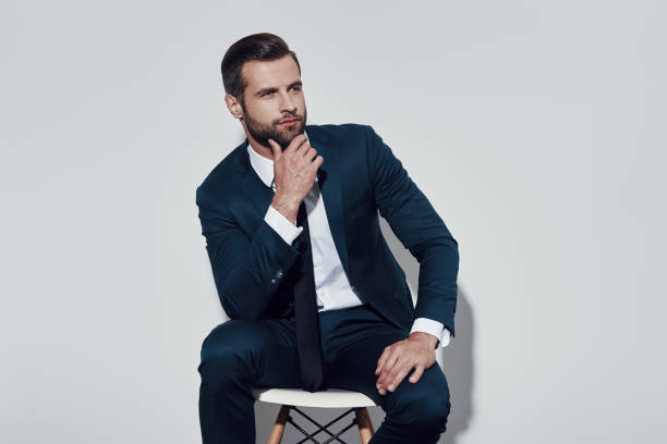 istock Looking into exciting future. Handsome young man looking away and keeping hand on chin while sitting against grey background 1155179289