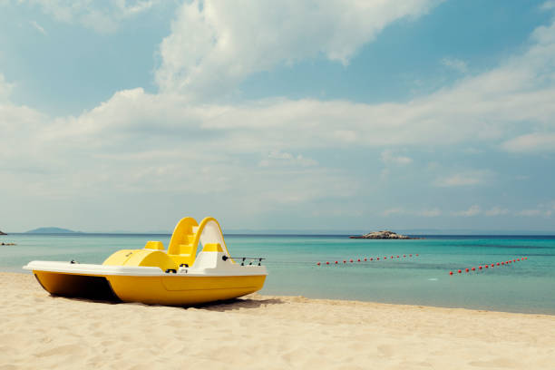 Yellow pedal boats on a turquoise beach in Greece and lines with red buoys Selective focus Yellow pedal boats on a turquoise beach in Greece and lines with red buoys Selective focus paddleboat stock pictures, royalty-free photos & images