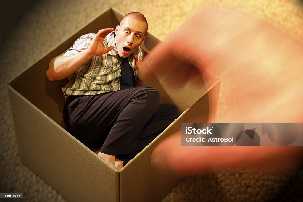 Little Man Trapped in a Box Do you ever feel like you're an inch tall, backed into a corner and everyone is out to get you? An imaginative scene of an anxious businessman trapped in a box with a giant’s hand trying to grab him. Men Stock Photo